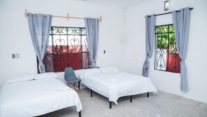 Une chambre avec deux lits simples, une chaise et une fenêtre avec des barreaux en métal.