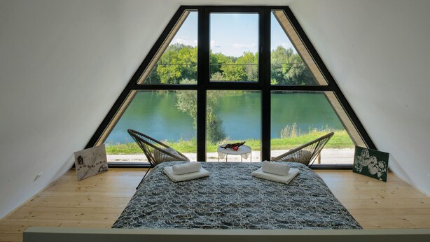 A bedroom with a large window overlooking a lake, two chairs, and a bed with towels. - 2 bedroom cozy home in Brodani (Brodani)