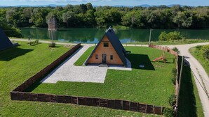 A triangular wooden cabin with a paved entrance area, surrounded by a wooden fence, near a lake with a clear sky and distant mountains. - 2 bedroom cozy home in Brodani (Brodani)