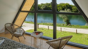 A room with a large window overlooking a lake, two wicker chairs, a small table with a heart-shaped object, and a patterned bedspread. - 2 bedroom cozy home in Brodani (Brodani)