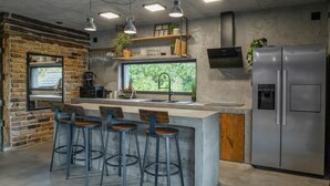 Una cocina moderna con pared de ladrillo, un ventanal grande, un refrigerador de acero inoxidable y taburetes de bar.