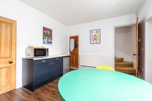 A compact kitchen with a microwave, a sink, and a dining area with a table and chairs. There is a staircase leading to another level.