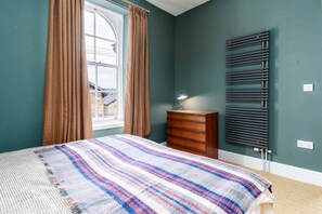A bedroom with a bed, a dresser, a radiator, and a window with curtains.