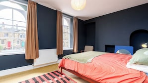 Quarto com cama, janela com cortinas, radiador, cadeira e abajur.