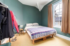 Un dormitorio con cama, una mesita de noche con lámpara, una silla y un ventanal con cortinas.