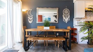 A dining area with a wooden table and benches, a large mirror on the wall, and decorative wall hangings.