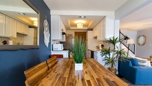 A modern kitchen with white cabinets, a wooden dining table, and a large plant in the center.