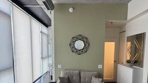 Ein geräumiges Wohnzimmer mit einem beigefarbenen Sofa, einem gemusterten Teppich und einem geometrischen Wandspiegel.