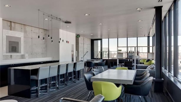 Ein moderner Konferenzraum mit einem langen Tisch und Stühlen, einer Küchenzeile mit einer Bar und großen Fenstern mit Blick auf die Stadt.