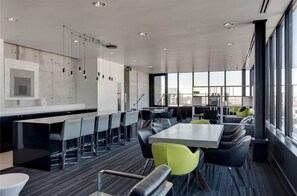 A modern conference room with a long table and chairs, a kitchen area with a bar, and large windows offering a city view. - Downtown Glasshouse Condo - 1 BR/1 Bath (Winnipeg)