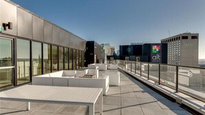 Eine Dachterrasse mit Sitzgelegenheiten im Freien und Blick auf die Stadt, sowie das Gebäude des Alt Hotels.