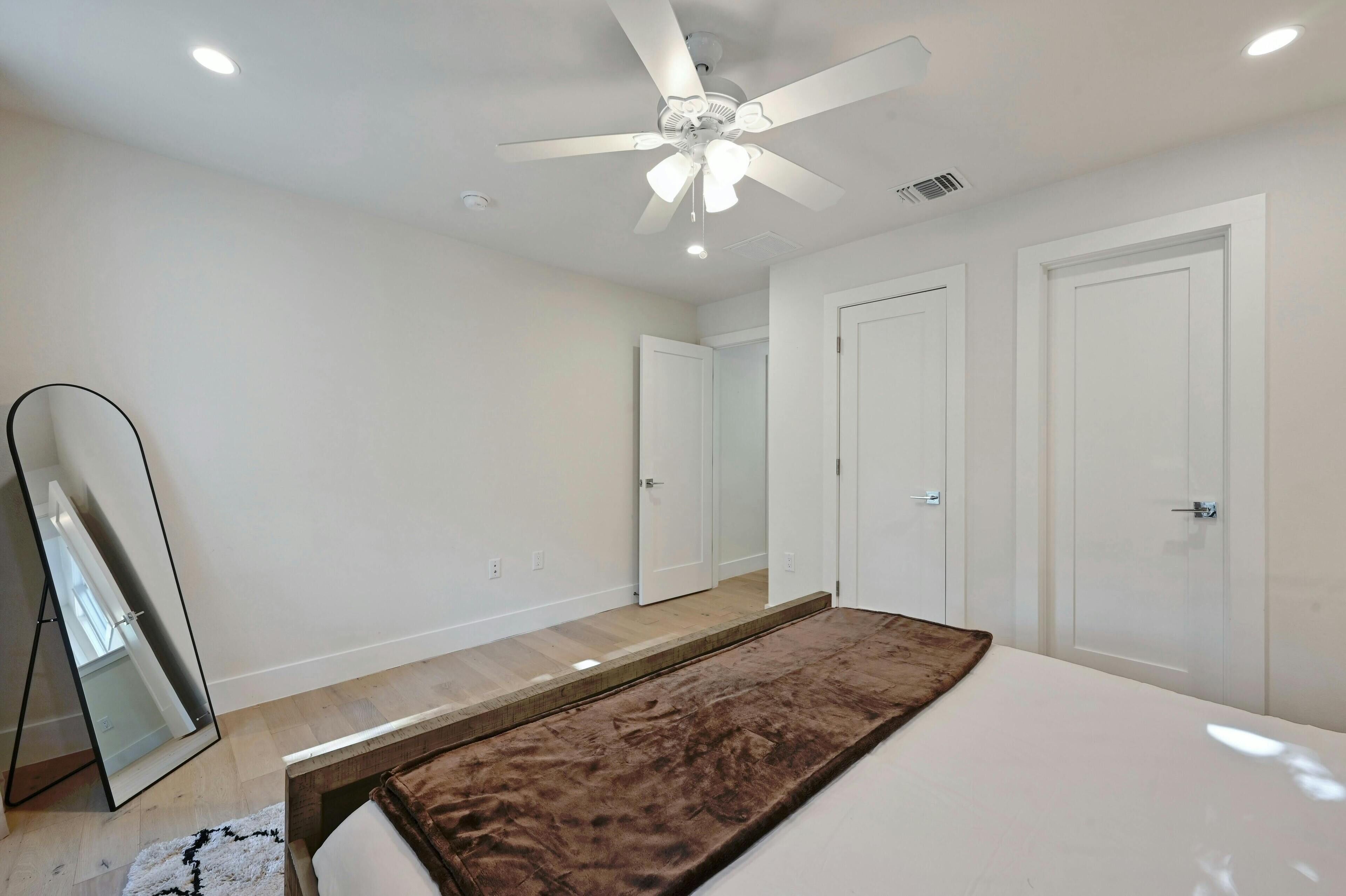 A bedroom with a bed, a ceiling fan, a large mirror, and white doors.