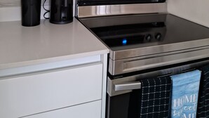 Una cocina con un microondas, horno y estufa de acero inoxidable. Hay un recipiente negro para utensilios, utensilios y una toalla azul colgada del mango del horno.