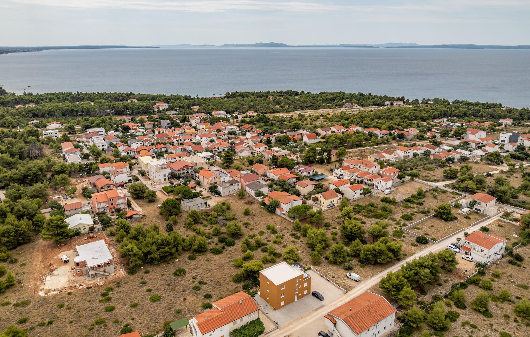 An aerial view of a coastal residential area with houses, some with red roofs, and a large body of water in the background.