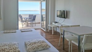 Habitación de hotel con cama, escritorio, televisor y balcón con vista al mar.