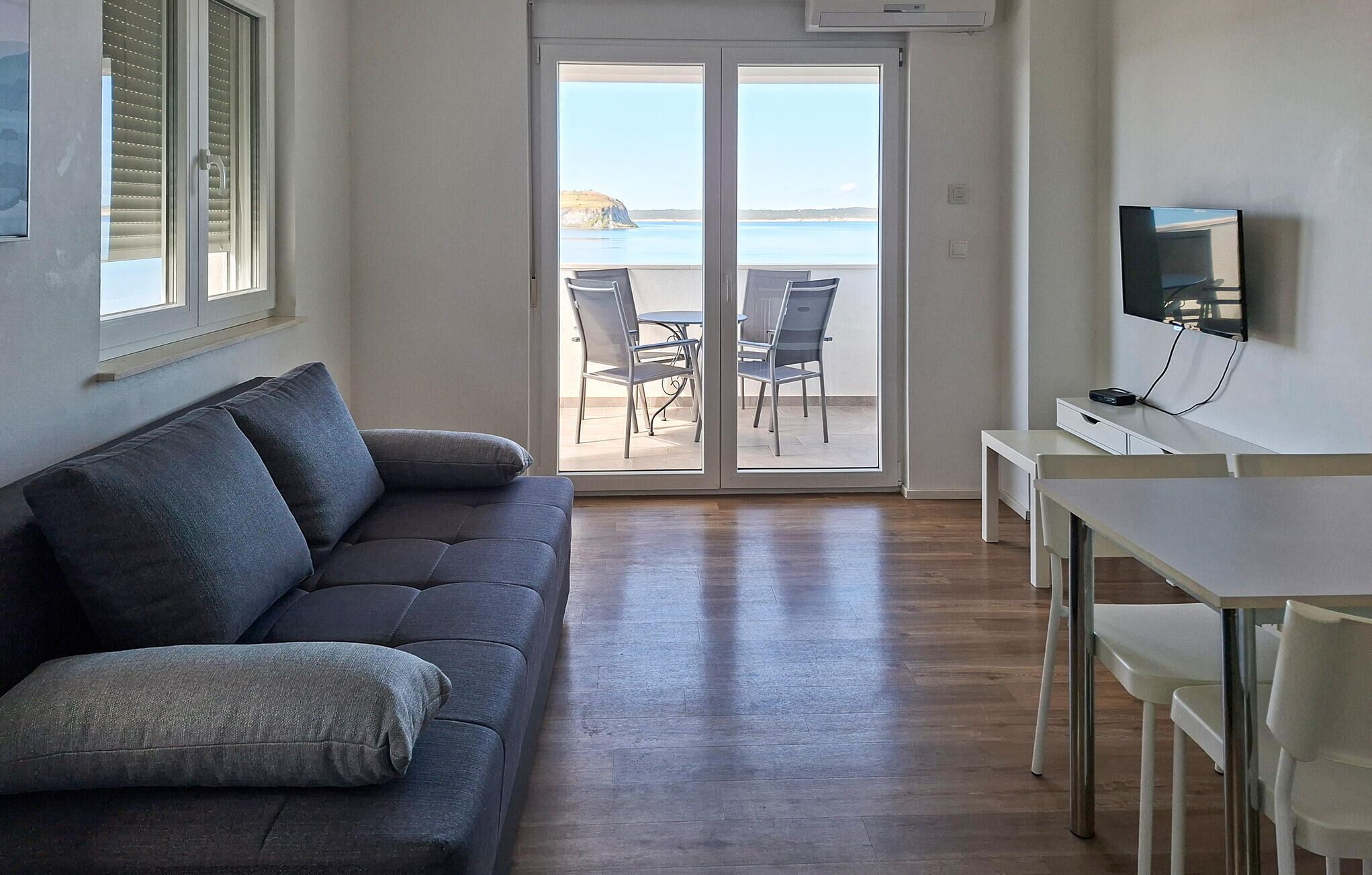 Een woonkamer met een bank, een televisie en een balkon met uitzicht op zee.
