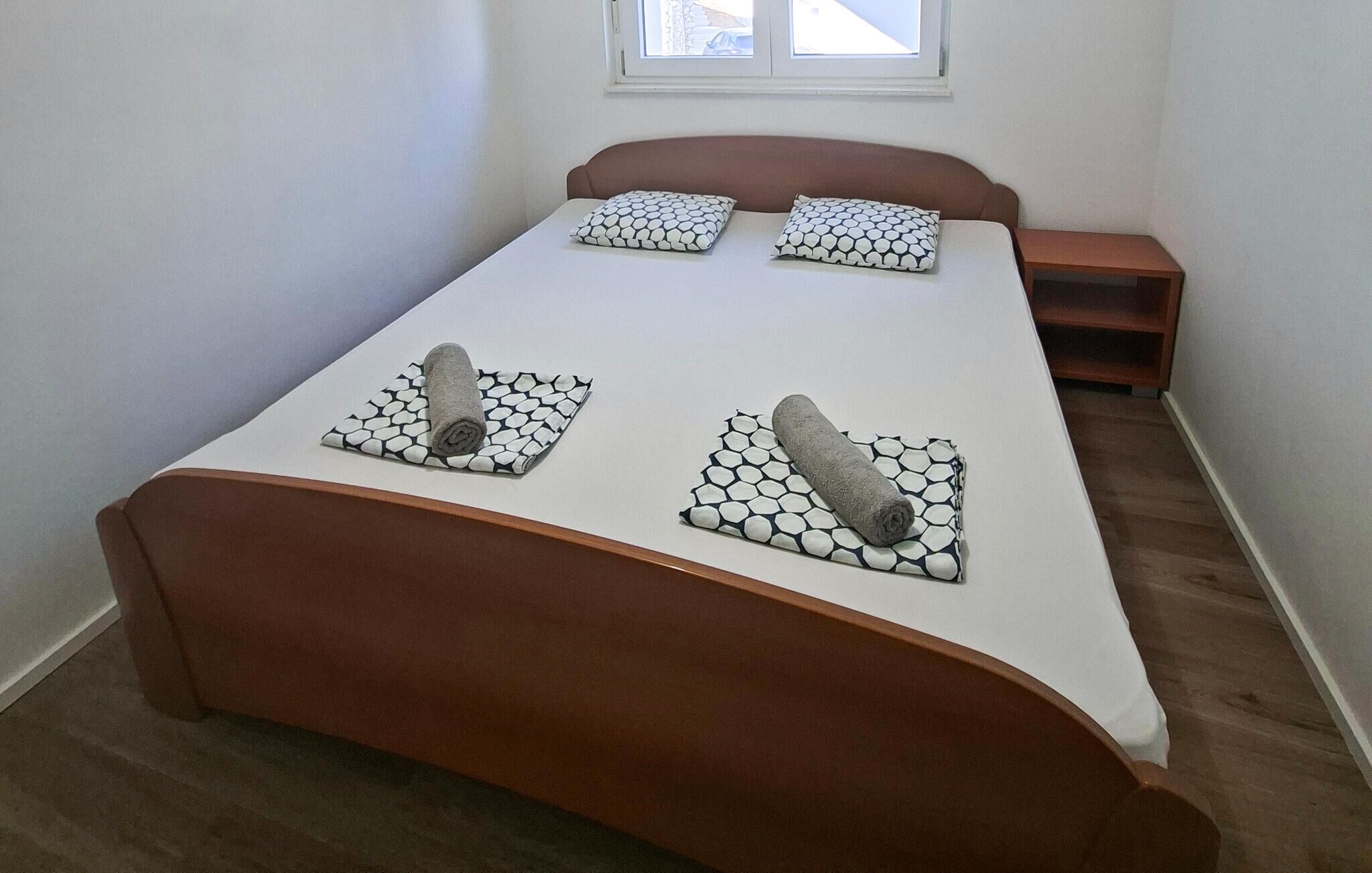 A bedroom with a bed, pillows, a bedside table, and a window.