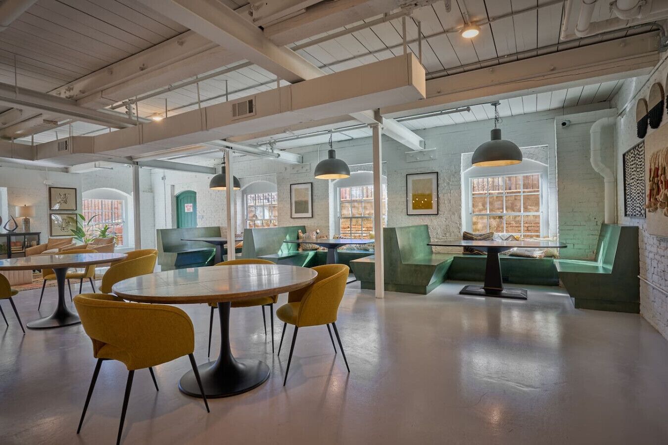 A spacious, well-lit interior with high ceilings, exposed ductwork, and a mix of seating areas including tables and couches.