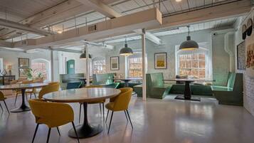 A spacious, well-lit interior with high ceilings, exposed ductwork, and a mix of seating areas including tables and couches.