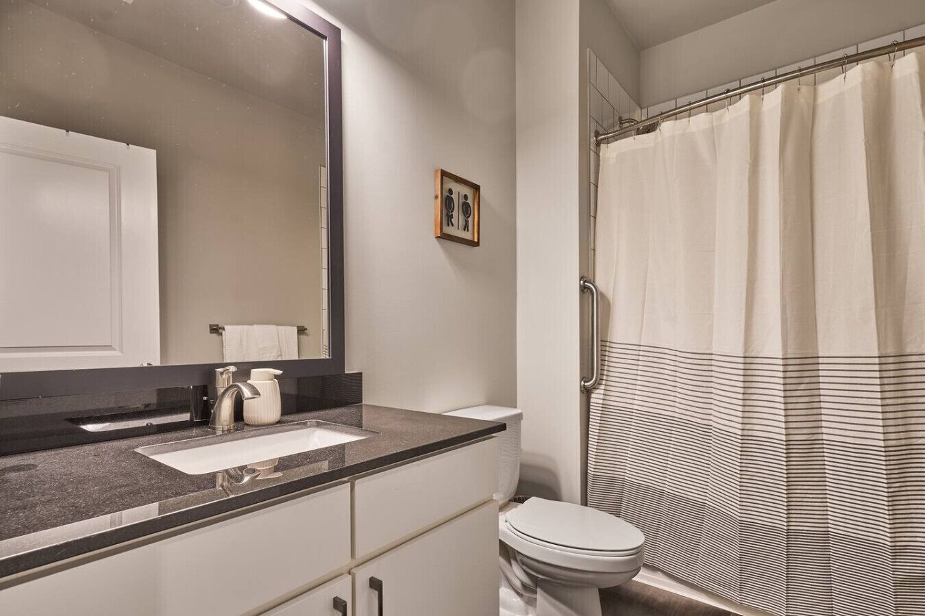 Un baño con un espejo grande, un lavamanos, un inodoro y una ducha con cortina a rayas.