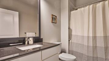 Un baño con un espejo grande, un lavamanos, un inodoro y una ducha con cortina a rayas.