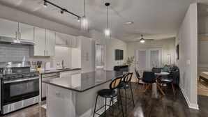 A modern kitchen with a central island, bar stools, and a dining area with a table and chairs. - Stylish, Cozy 2BD Apt Near DT Clayton | Pool | Gym (Clayton)