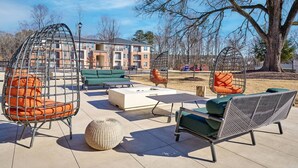 An outdoor seating area with various chairs and a sofa, a round table, and a large tree in the background. - Stylish, Cozy 2BD Apt Near DT Clayton | Pool | Gym (Clayton)