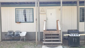 A covered porch with a wooden staircase leading to a door, a barbecue grill, and two metal chairs. - 3-bedroom mobile home in fabulous Coffee Creek (Trinity Center)