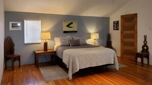 A bedroom with a bed, two bedside tables, a nightstand, a window with blinds, a door, and a wall-mounted picture. - Penthouse apartment in a charming barn in La Union- perfect for a cozy getaway (Anthony)