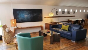 A modern living room with a blue sofa, a green armchair, a wooden coffee table, and a large abstract painting on the wall. - Penthouse apartment in a charming barn in La Union- perfect for a cozy getaway (Anthony)