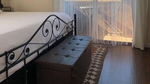 Un dormitorio con cama, banco y cortinas.