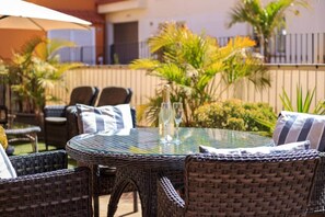 Eine Terrasse im Freien mit Korbmöbeln, einem Glastisch und einer Champagnerflasche.