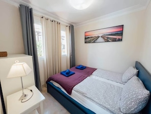 Ein Hotelzimmer mit einem Bett, einem Nachttisch mit Lampe, einem Fenster mit Vorhängen und einem Gemälde an der Wand.