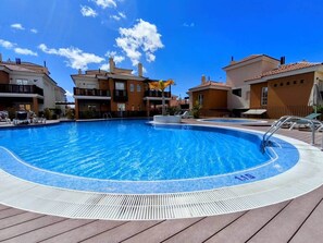 Une piscine dotée d’une terrasse carrelée, entourée d’immeubles avec des balcons, sous un ciel dégagé.