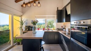 Une cuisine moderne dotée d’un grand îlot central, d’appareils électroménagers intégrés et offrant une vue sur la verdure.