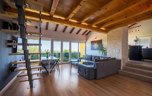 A modern living room with a wooden ceiling, a sofa, a dining table, and a staircase leading to an upper level.