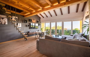 A modern living room with a wooden ceiling, a large TV, a dining area, and a sofa.
