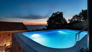 A swimming pool with a view of the sunset over the water, surrounded by stone walls and trees. - Awesome home in Prizna (Prizna)