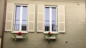 En bygnings facade med to vinduer, hver med hvide skodder og en lille altan.