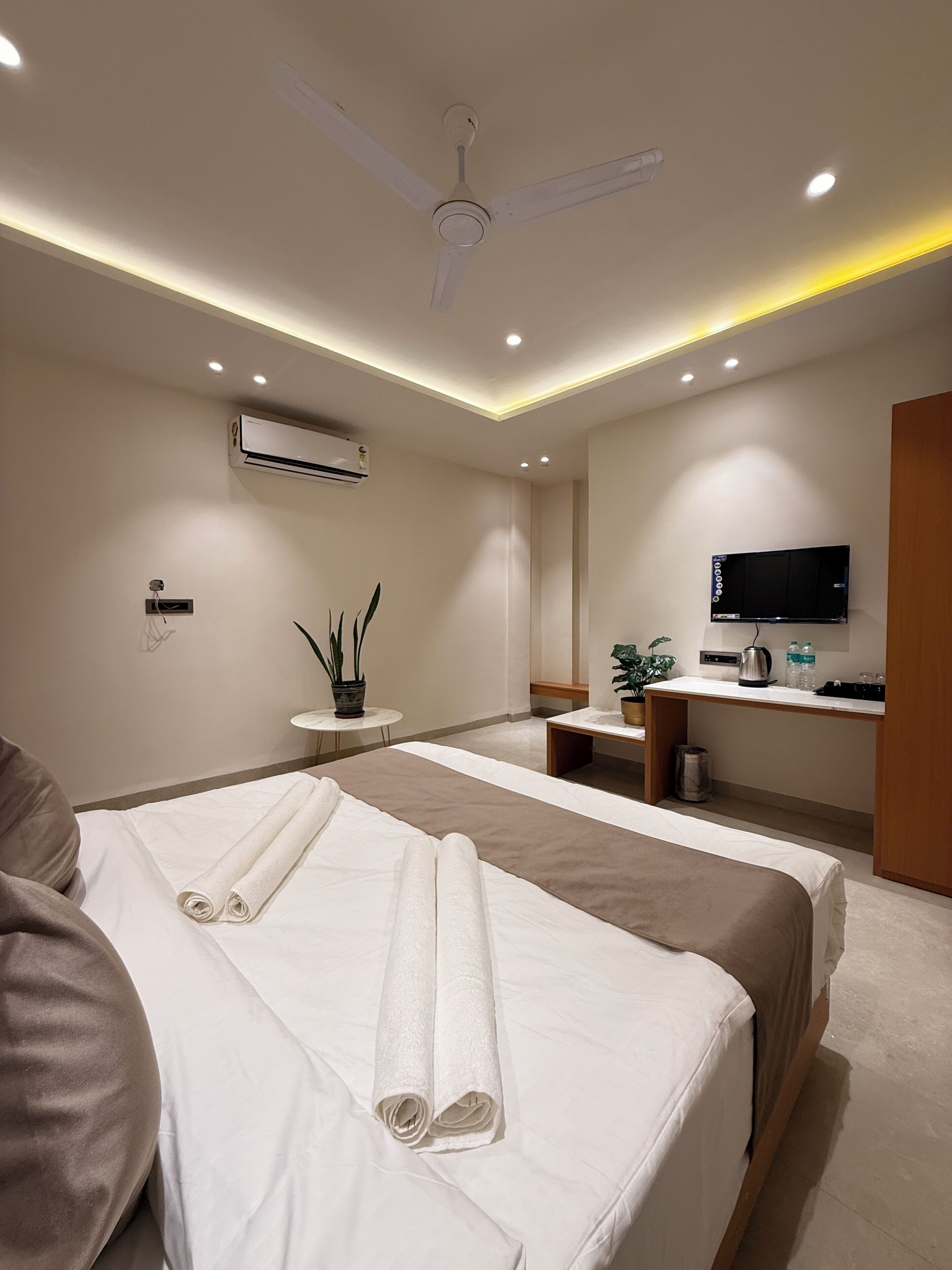 A hotel room with a bed, a desk, a television, an air conditioning unit, and a ceiling fan.