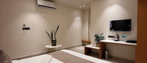 A hotel room with a bed, a desk, a television, an air conditioning unit, and a ceiling fan.