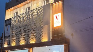 A hotel with a modern facade, a prominent 'V' sign, and a neon sign indicating 'HOTEL VIMLAYATAN'. - Hotel vimlayatan (Ujjain)