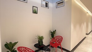 A corridor with two red chairs, a small table, and potted plants. - Hotel vimlayatan (Ujjain)