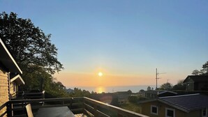 Eine Holzdar Terrasse mit Tisch und Stühlen, mit Blick auf ein Wohngebiet und einen Sonnenuntergang.