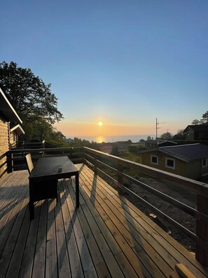A wooden deck with a table and chairs, overlooking a residential area and a sunset.