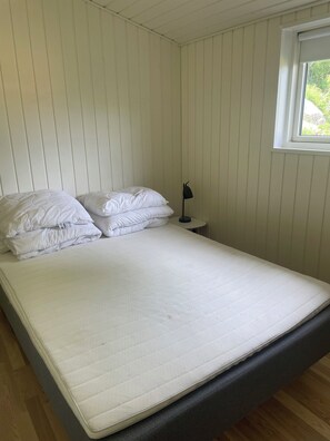 A single bed with white bedding, a bedside lamp, and a window with a view of greenery. - Cottage with a View- 5 min from beach (Allinge)