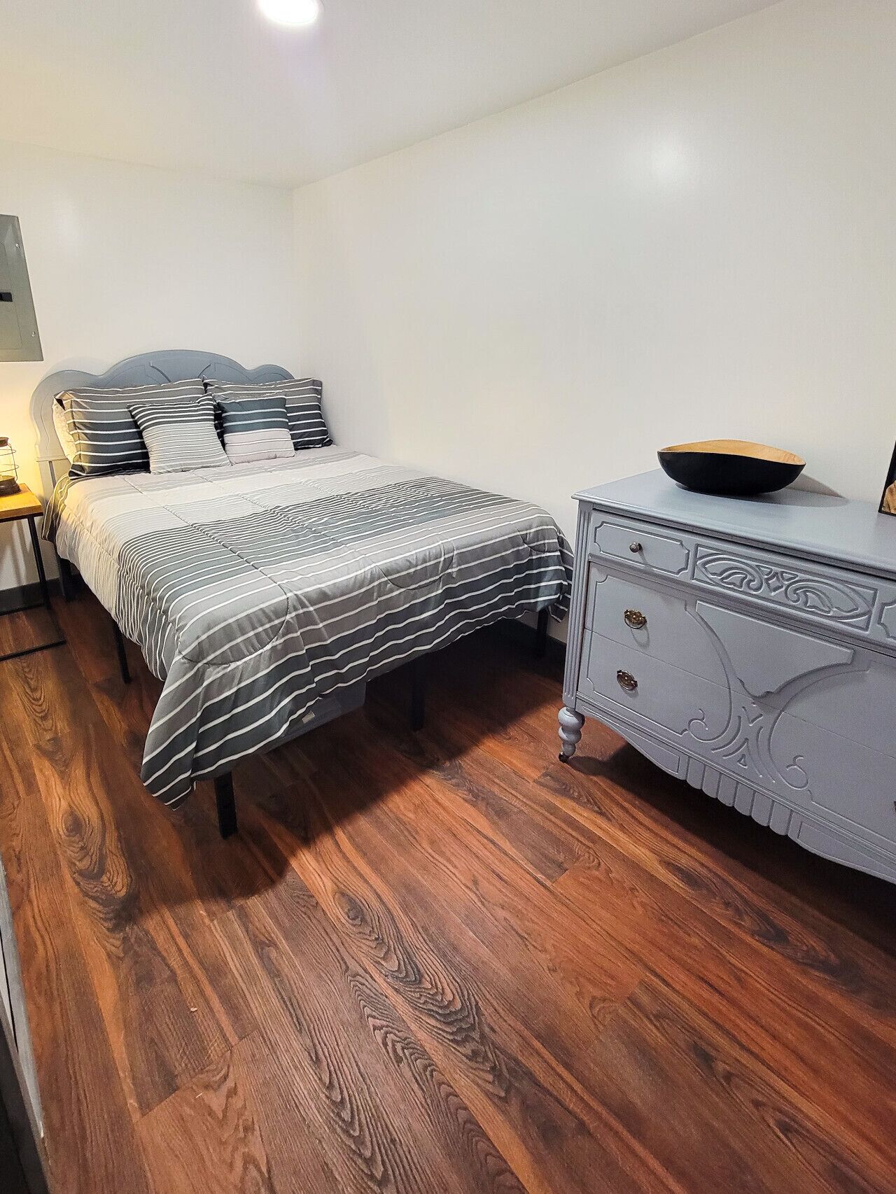 A bedroom with a bed, a nightstand, a dresser, and a wooden floor.