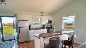 A modern kitchen with white cabinets, a stainless steel refrigerator, a microwave, and an island with two bar stools. - Fun for the whole Family with a beautiful view! (French River)