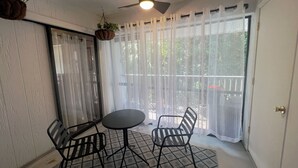 Ein kleiner, abgeschlossener Balkon mit Tisch und zwei Stühlen, einem Deckenventilator und Blick durch transparente Vorhänge.