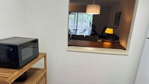 Eine kompakte Küche mit einer Mikrowelle auf einem Holztisch, ein kleiner Essbereich mit Tisch und Stühlen sowie ein Blick ins Freie durch ein Fenster.